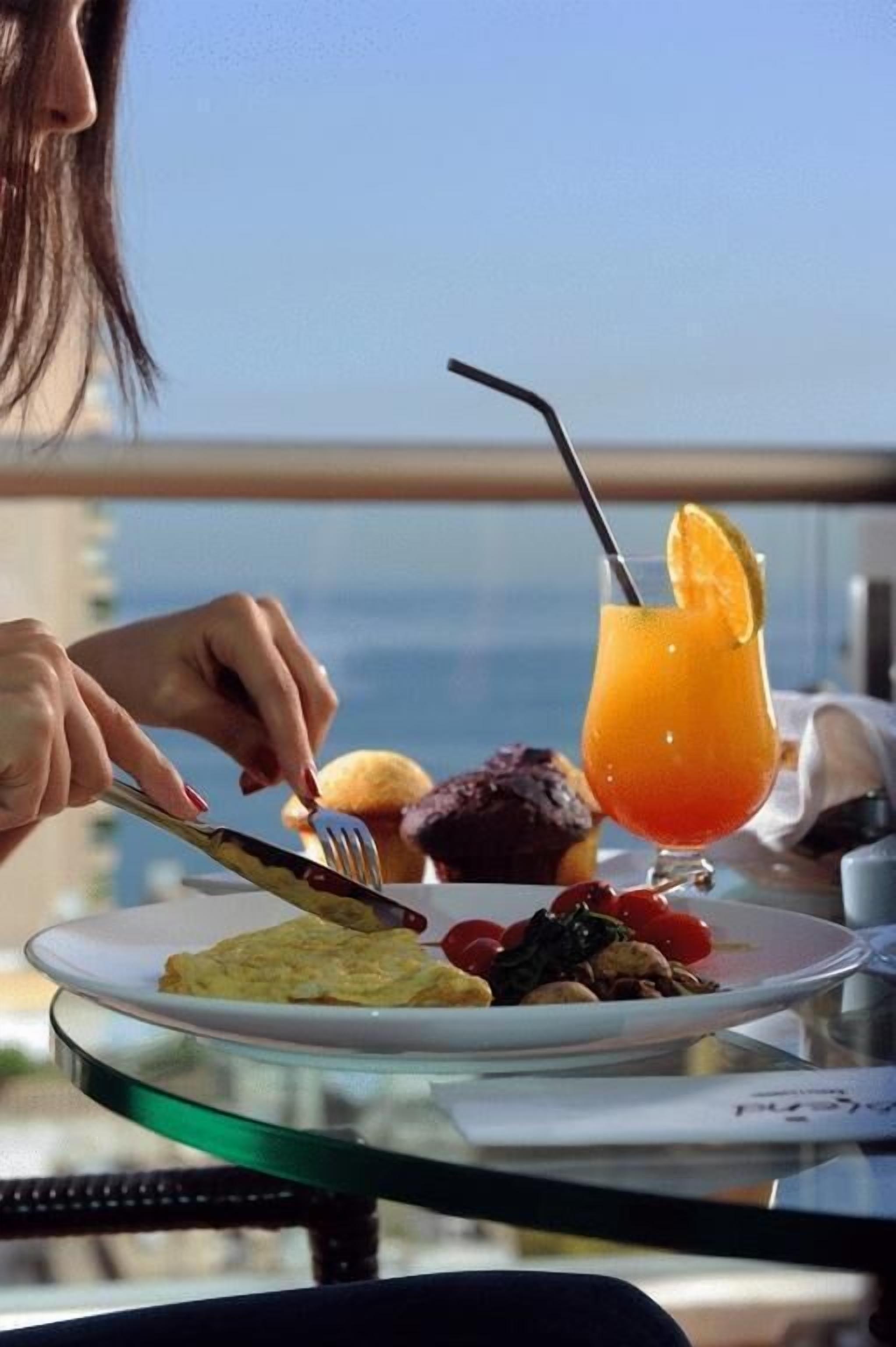 A person dining at a table with a glass of orange juice and a plate of food.
