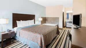 Habitación de hotel con cama, televisor, baño y escritorio con lámpara.