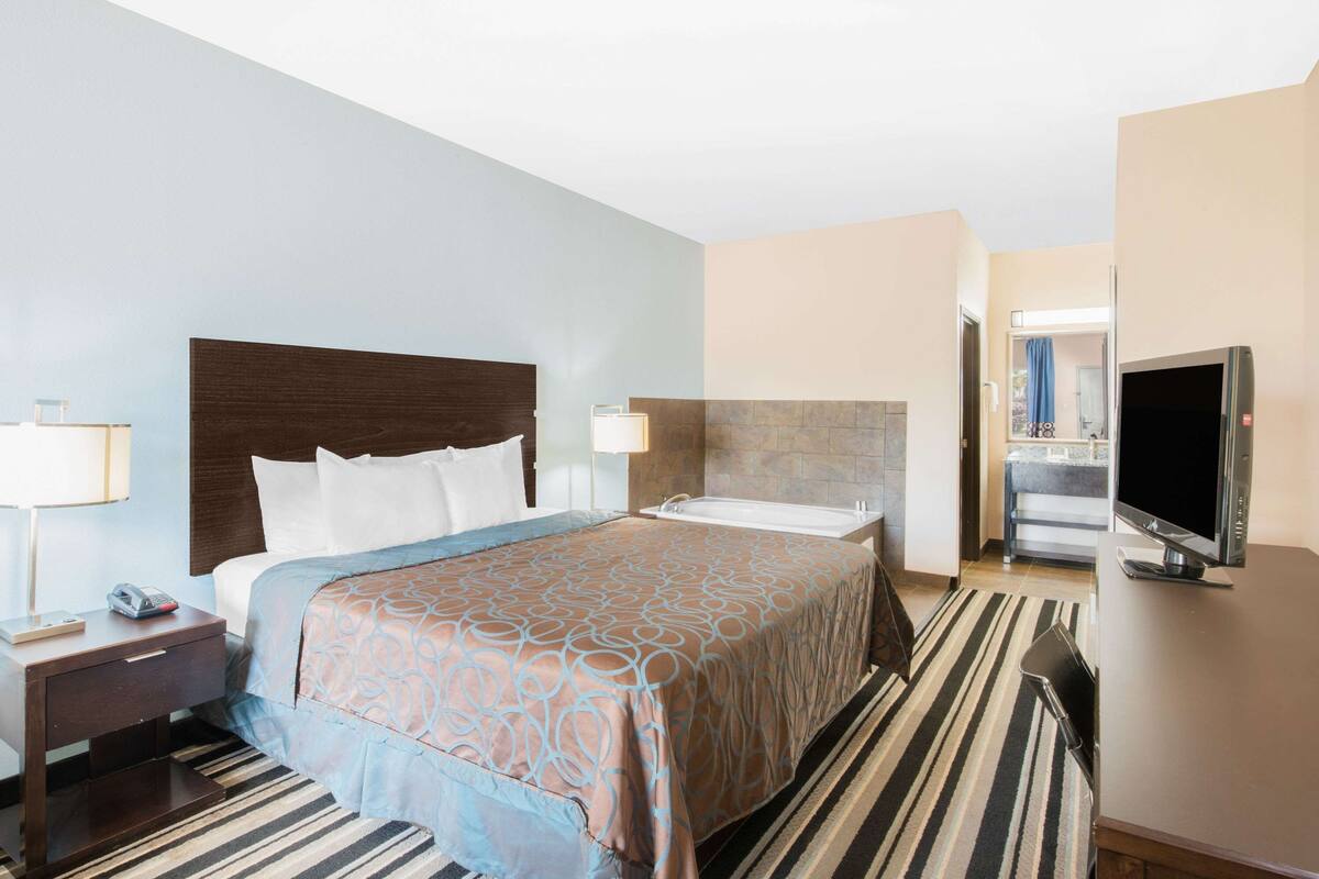 Een hotelkamer met een bed, televisie, badkamer en bureau met lamp.
