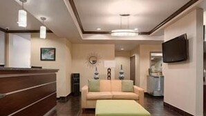 Un hall de hotel con mostrador de recepción, un sofá, un reposapiés, un televisor y un adorno de pared.