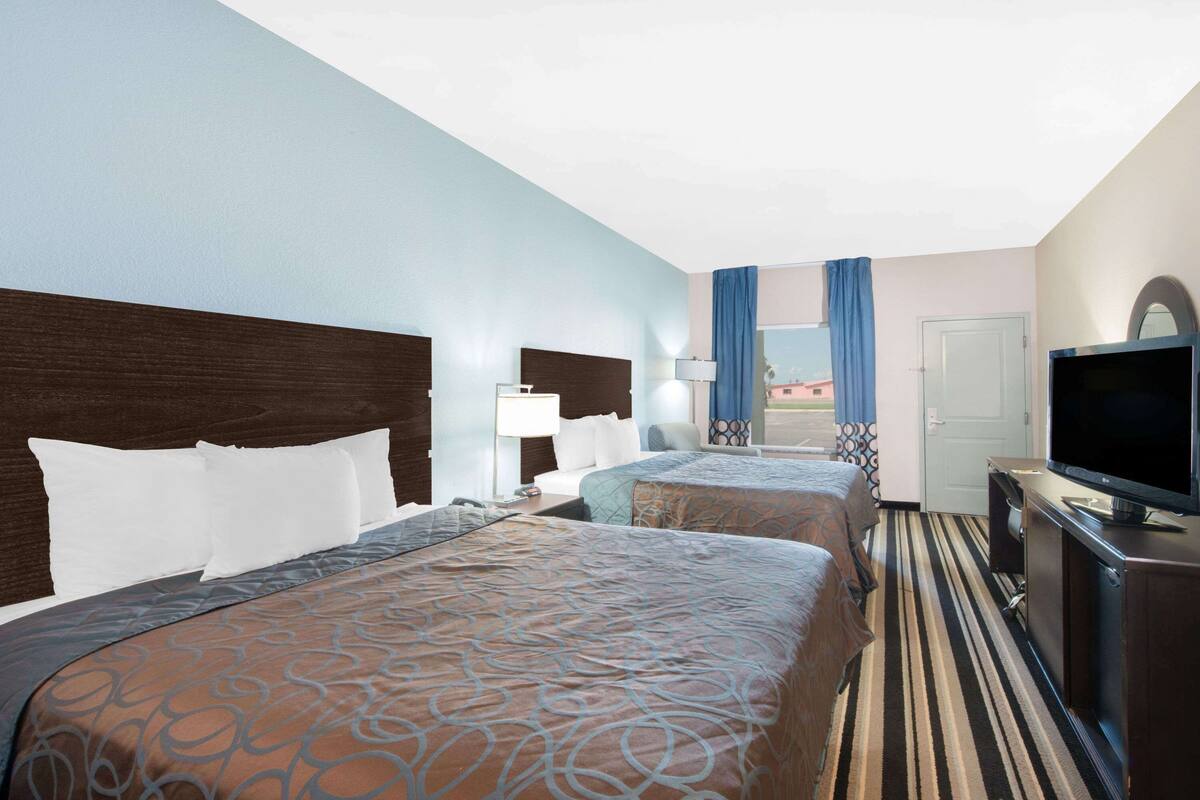 Een hotelkamer met twee bedden, een televisie, een bureau en een raam met gordijnen.