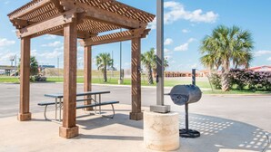 Una pérgola de madera con bancos y una parrilla en un parque.