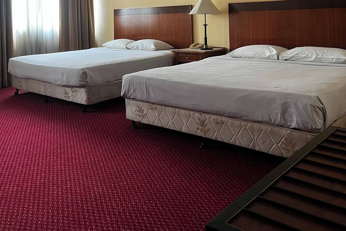 A hotel room with two beds, a wooden headboard, a nightstand with a lamp, and a framed picture on the wall.