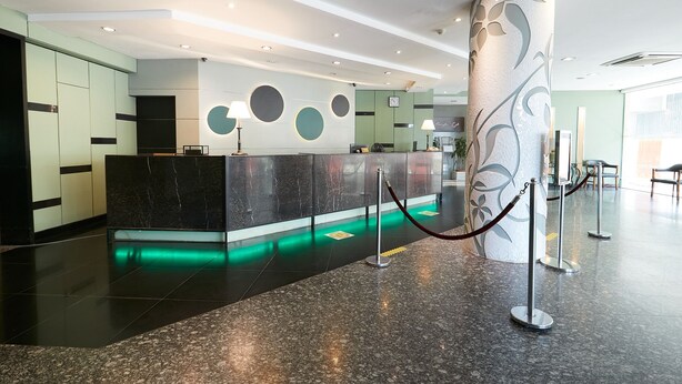 A modern reception area with a marble counter, green and black decor, and a glass partition. - Grand Pacific Hotel PWTC (Kuala Lumpur)