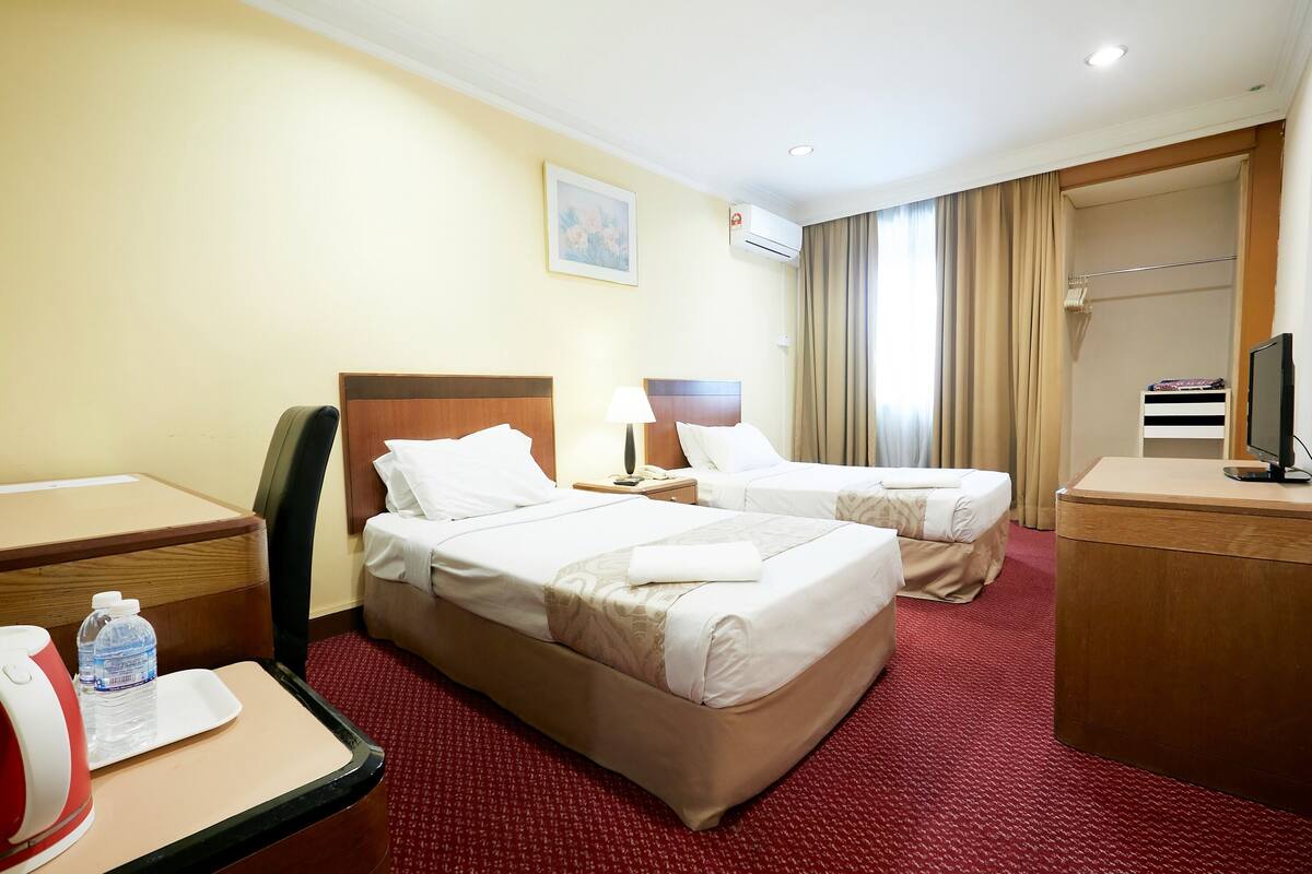 A hotel room with two beds, a desk, a chair, a TV, and a bathroom with a shower curtain.