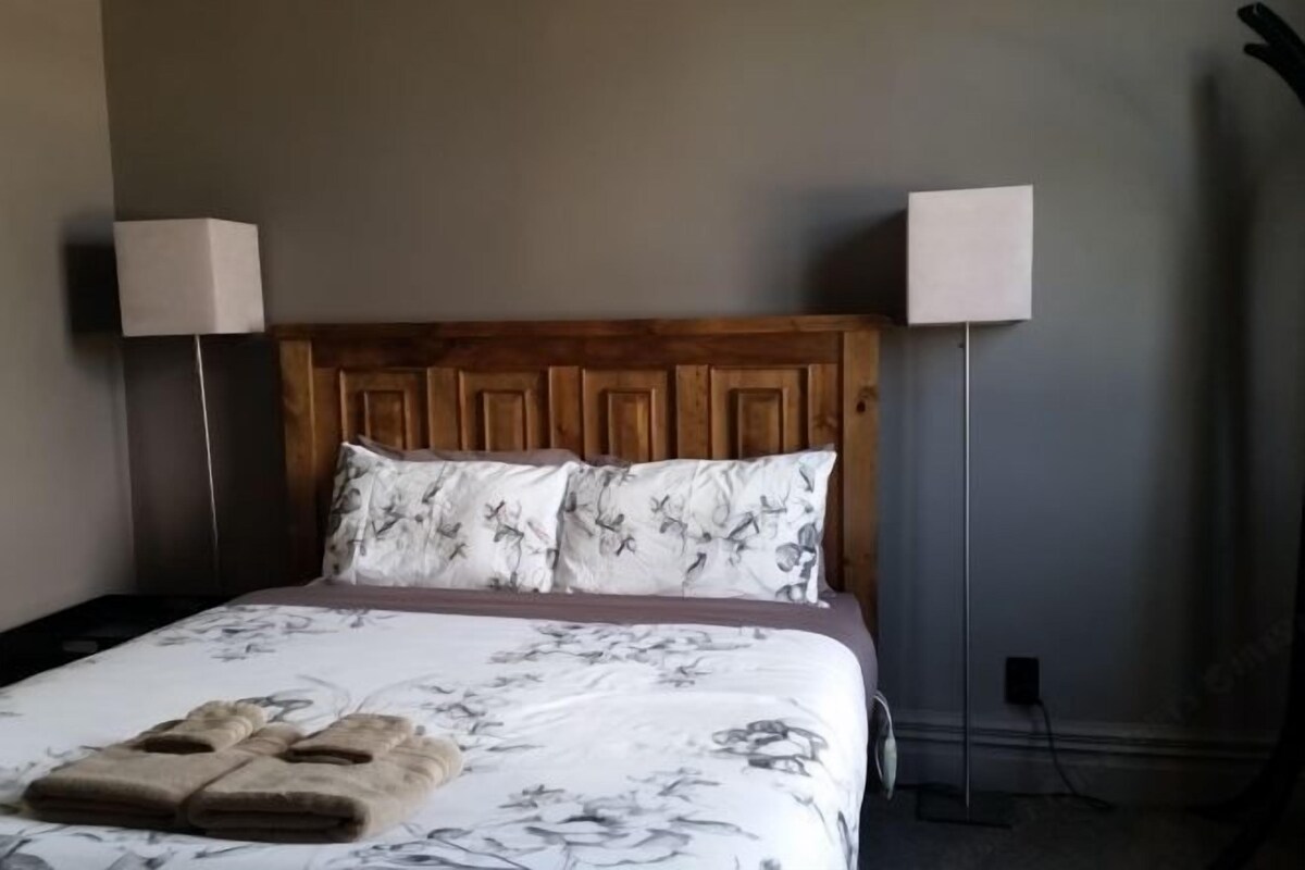Un lit bien fait, avec une literie à motifs floraux, deux lampes de chevet et une paire de serviettes pliées posées sur le lit.