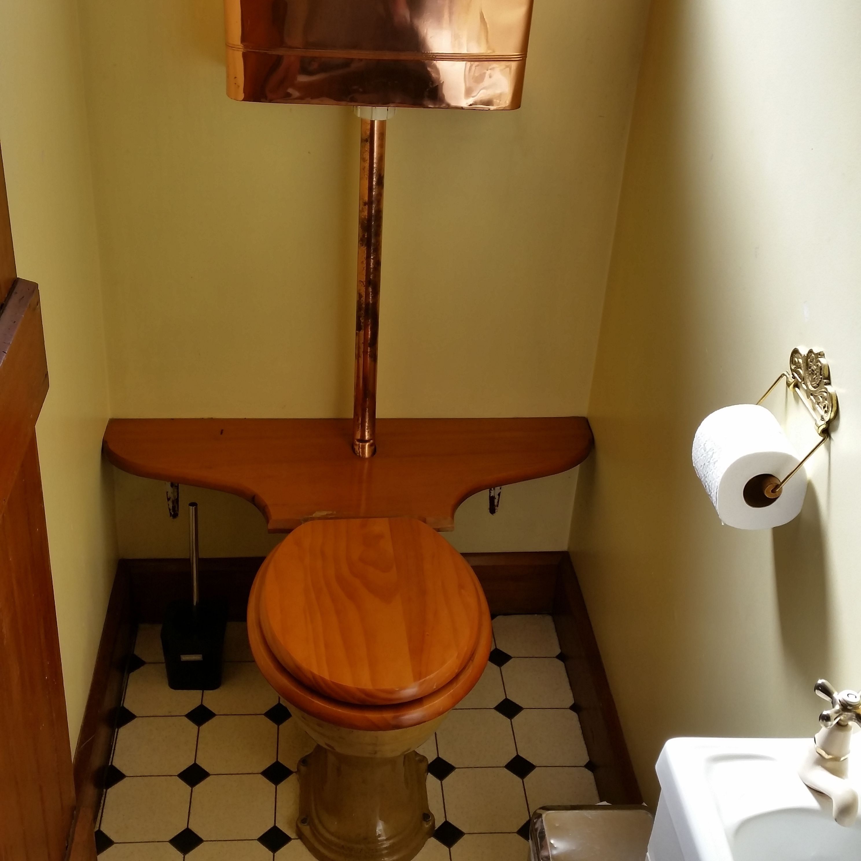 Een badkamer met een houten toilet, een witte wastafel en een toiletrolhouder aan de muur.