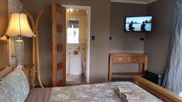 A hotel room with a bed, a TV mounted on the wall, a wooden nightstand, a lamp, and a door leading to a bathroom.