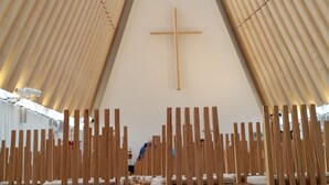 A church interior with wooden pews arranged in rows, a central wooden cross on the wall, and a high, sloped ceiling. - Designer Cottage B&B (Christchurch)