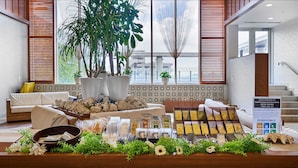 A hotel lobby with a reception desk, a sofa, a large potted plant, and a staircase.