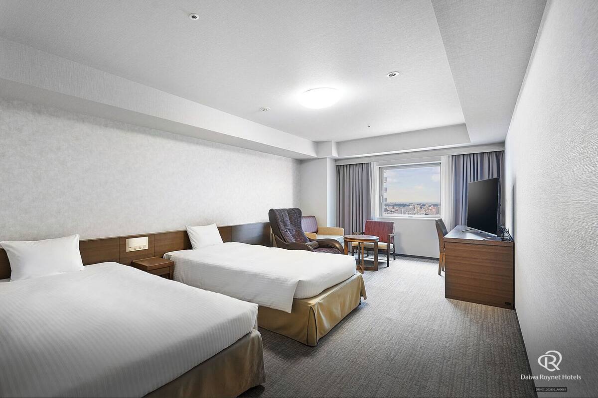 A hotel room with two beds, a desk, a chair, and a TV.