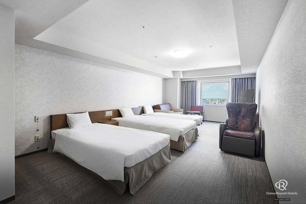 A hotel room with two beds, a desk, a chair, and a large window with a city view.