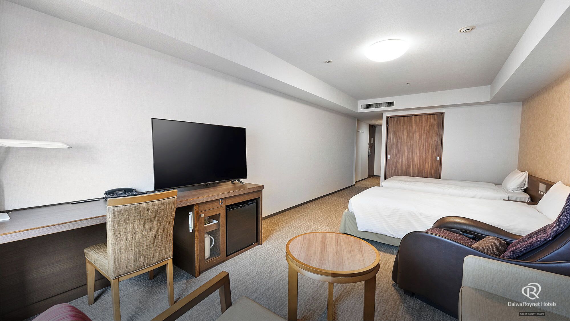 A hotel room with a flat-screen TV, a wooden cabinet, a small round table, a sofa, and a bed.
