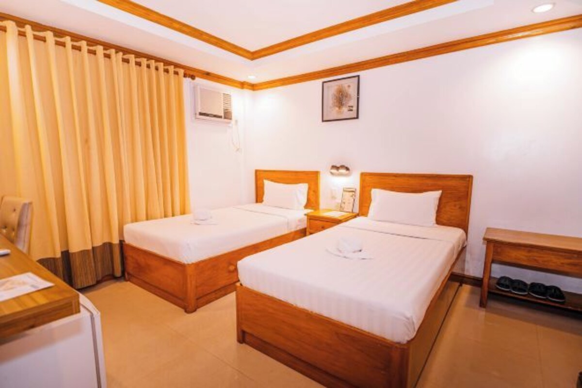 A hotel room with two beds, a desk, a chair, a small table, and a shoe rack.