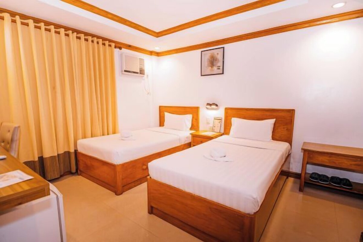 A hotel room with two beds, a desk, a chair, a small table, and a shoe rack.