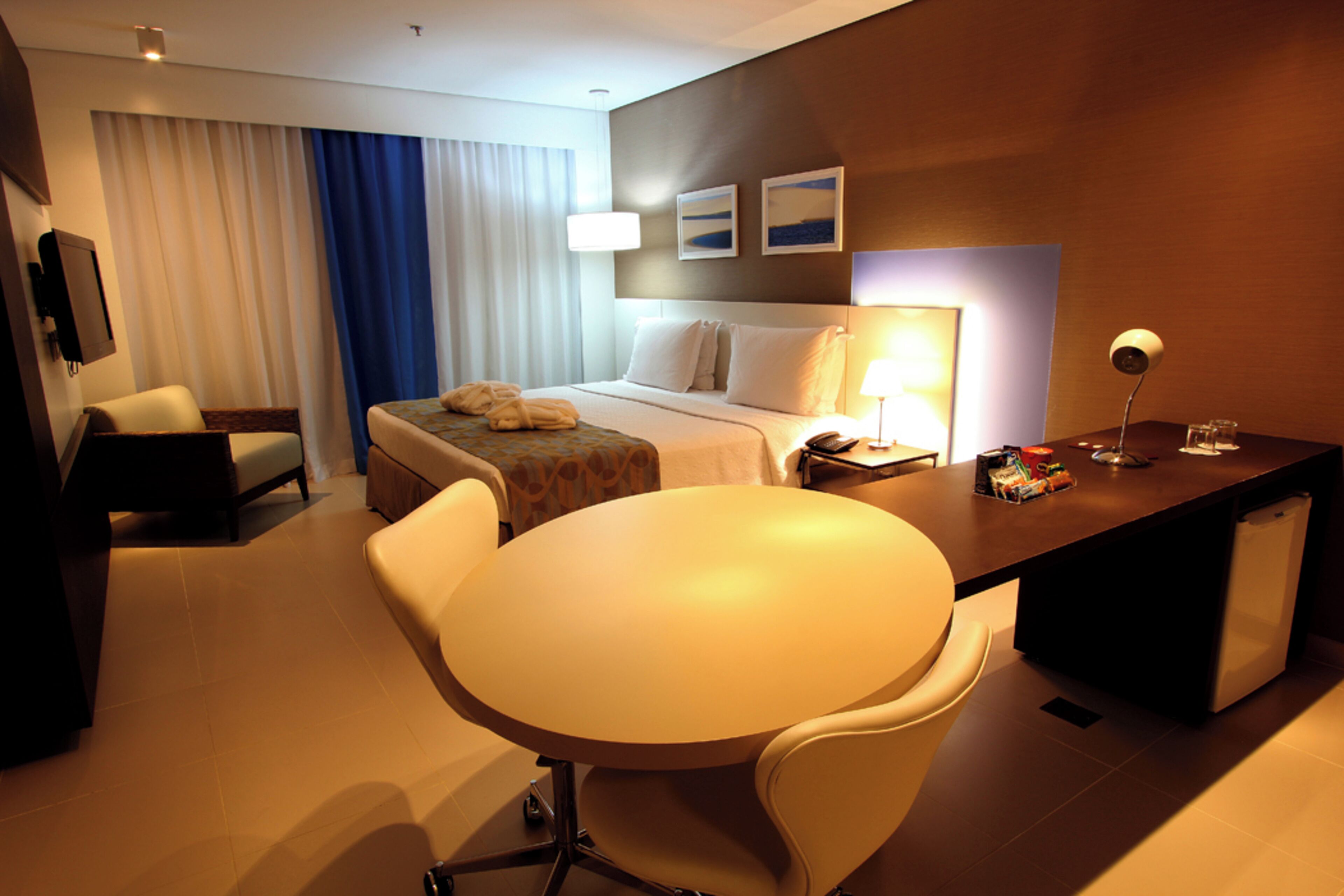 Habitación de hotel con cama, escritorio, silla, mesa, televisor y lámpara.