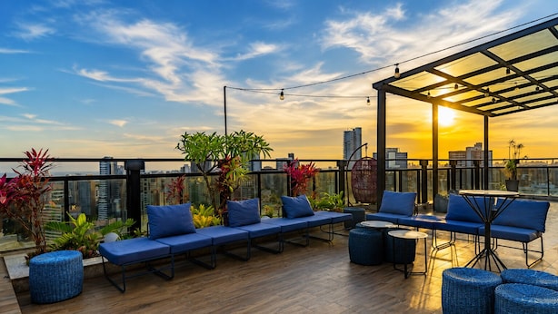 Eine Dachterrasse mit Holzboden, blauen Sitzmöbeln, einem runden Tisch und Topfpflanzen.