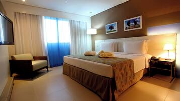 A hotel room with a bed, a chair, a desk, a TV, and a window with curtains.