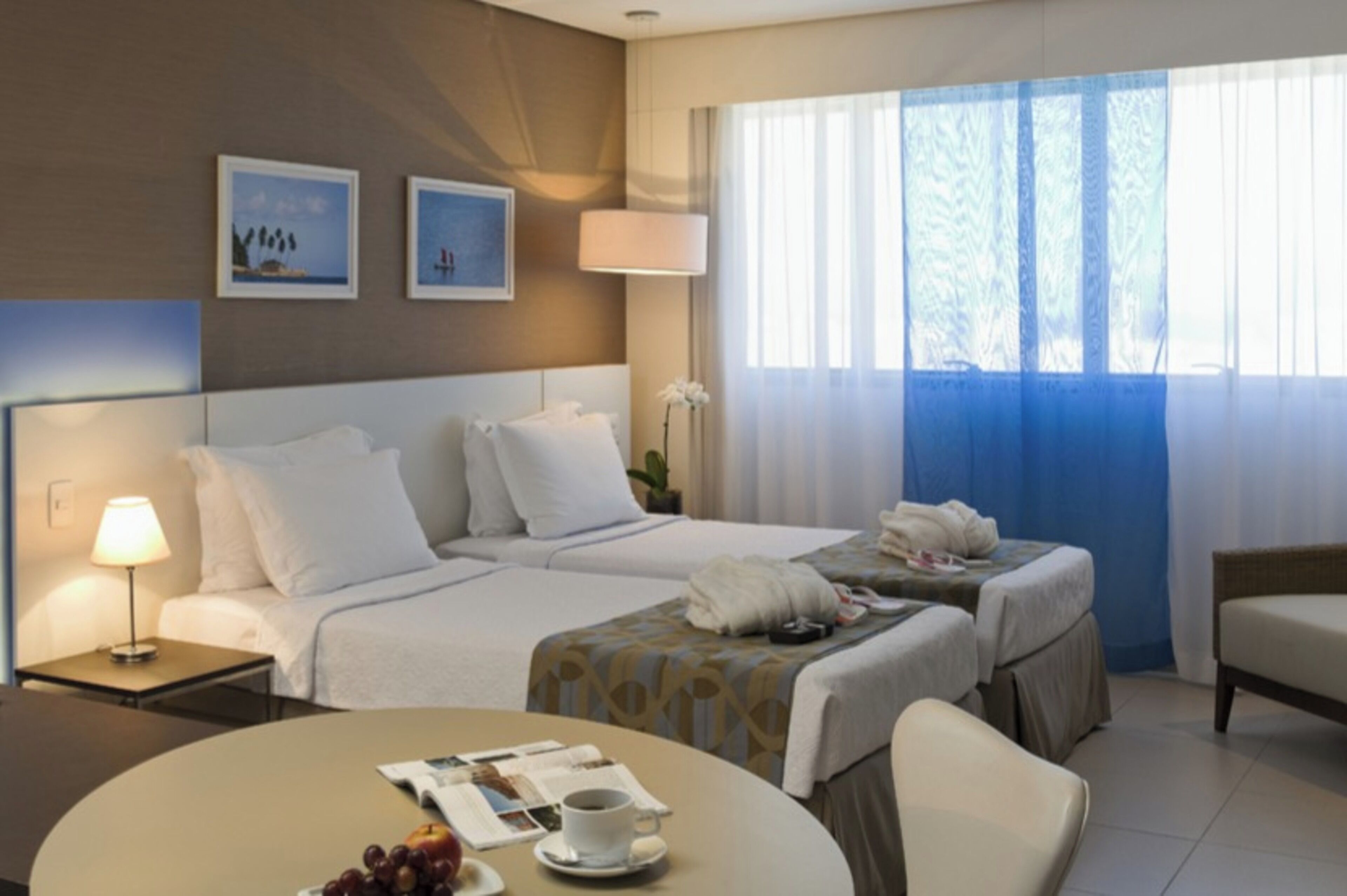 Een hotelkamer met twee bedden, een zithoek met een tafel, een lamp en een raam met gordijnen.