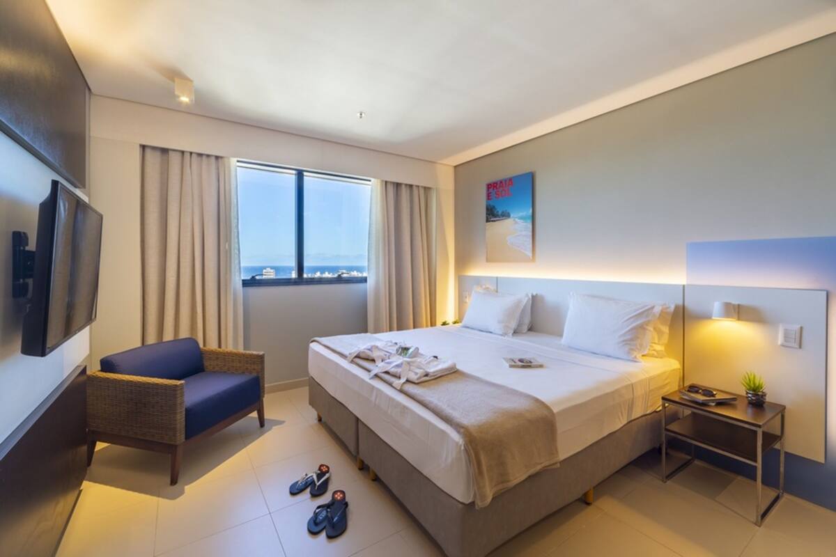 A hotel room with a bed, a chair, a nightstand, and a TV.