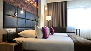A hotel room with a large bed, a headboard with built-in lighting, a bedside table with a phone, and a window with curtains. - Hotel Vestil (Piotrkow Trybunalski)