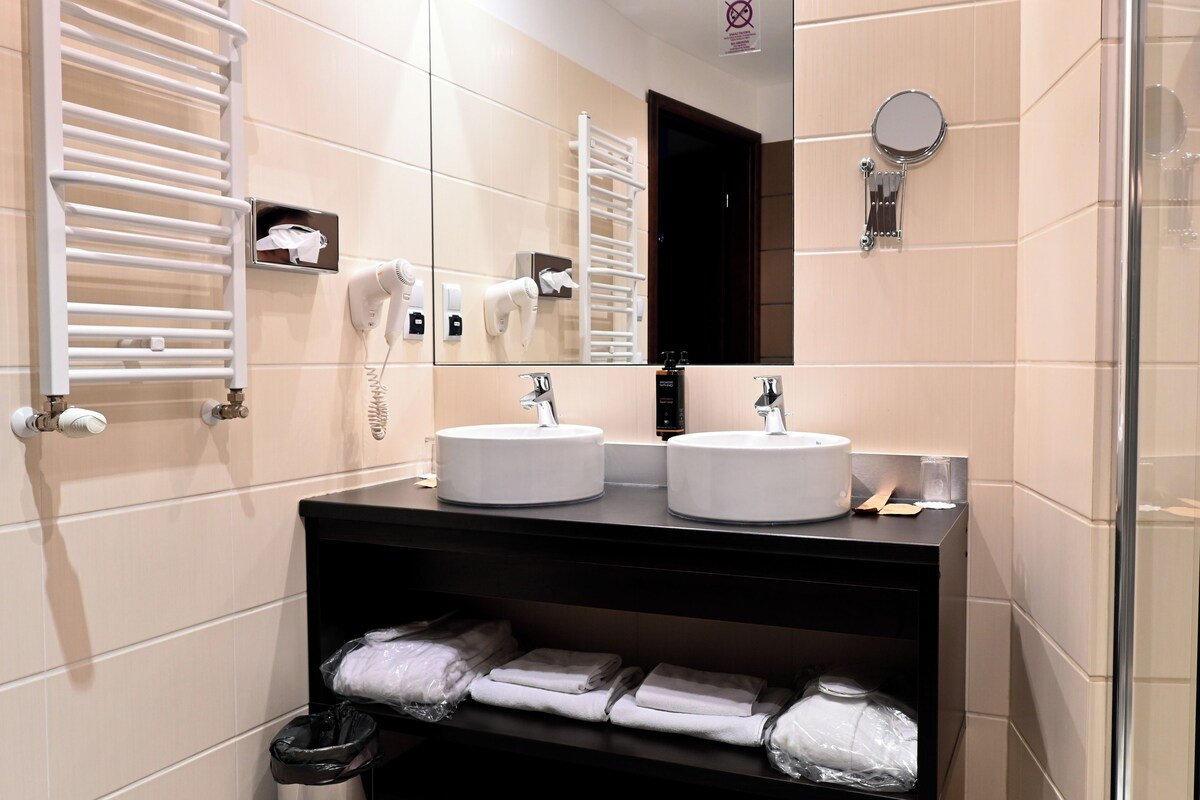 Une salle de bain avec deux lavabos, un miroir, un porte-serviettes et une cabine de douche en verre.