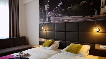 Habitación de hotel con dos camas, un sofá, un cartel grande con vistas de la ciudad y un cabecero moderno con iluminación integrada.