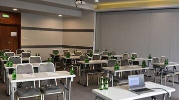 Un salón de conferencias con filas de mesas, sillas y botellas verdes.