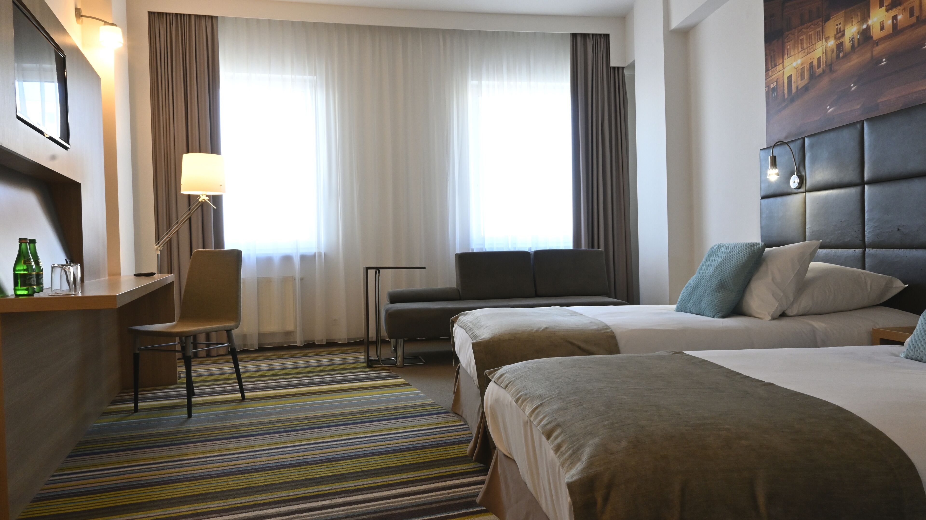 Une chambre d’hôtel avec deux lits, un bureau, une chaise, une lampe et une vue sur la rue par la fenêtre.