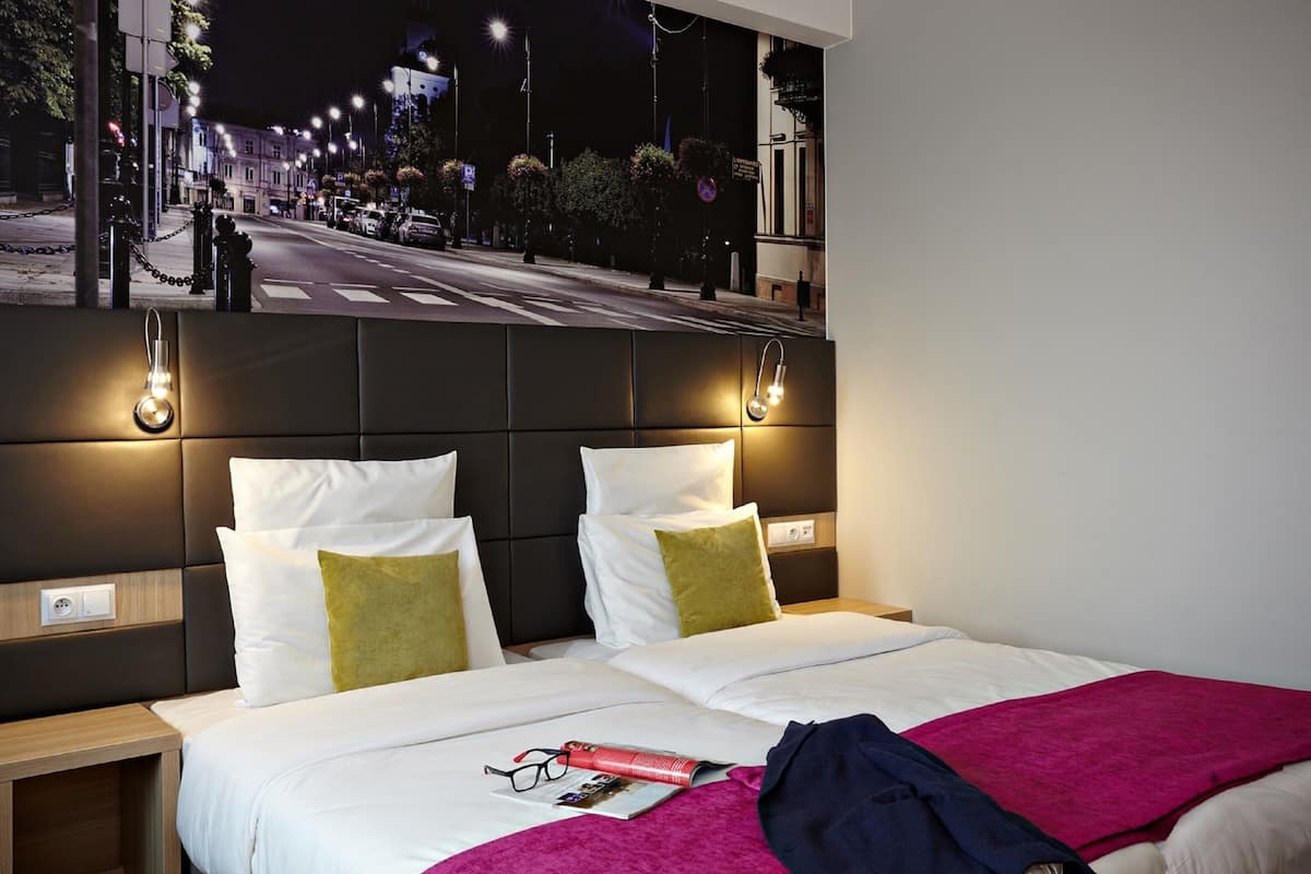 Une chambre d’hôtel avec un grand lit, deux tables de chevet et un luminaire fixé au mur.