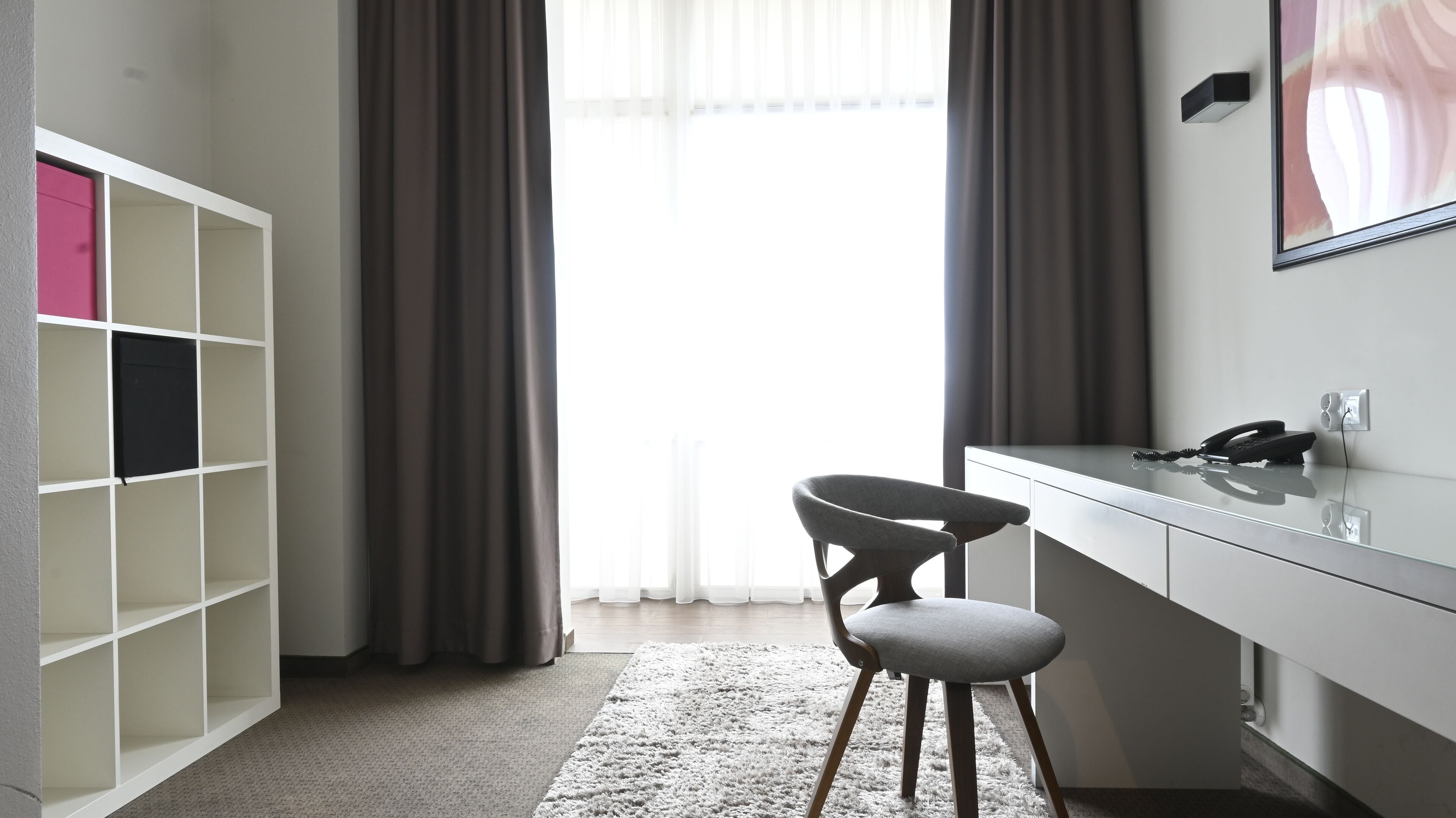 Ein modernes Zimmer mit Schreibtisch, Stuhl und einem weißen Regal.