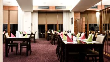 Une salle de conférence dotée de plusieurs tables et chaises, de grandes fenêtres et d’un plafond haut.