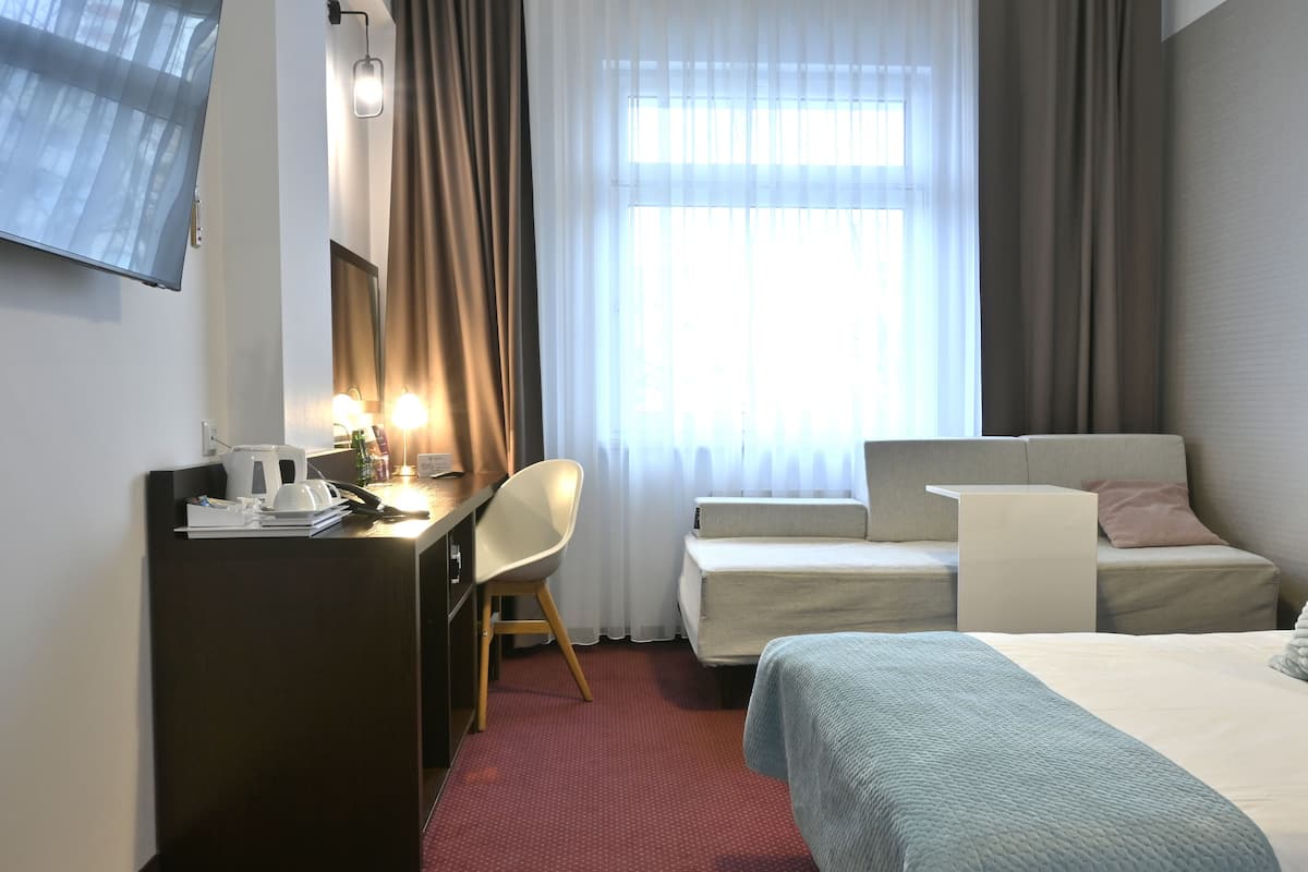 Une chambre d’hôtel avec un lit, un bureau et une chaise, une télévision et une fenêtre avec des rideaux.