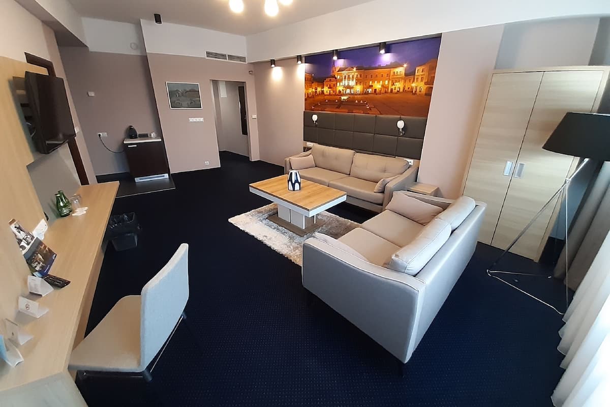 Une chambre d’hôtel moderne, équipée d’un canapé, d’une table basse, d’un téléviseur et d’un tableau représentant un paysage urbain.