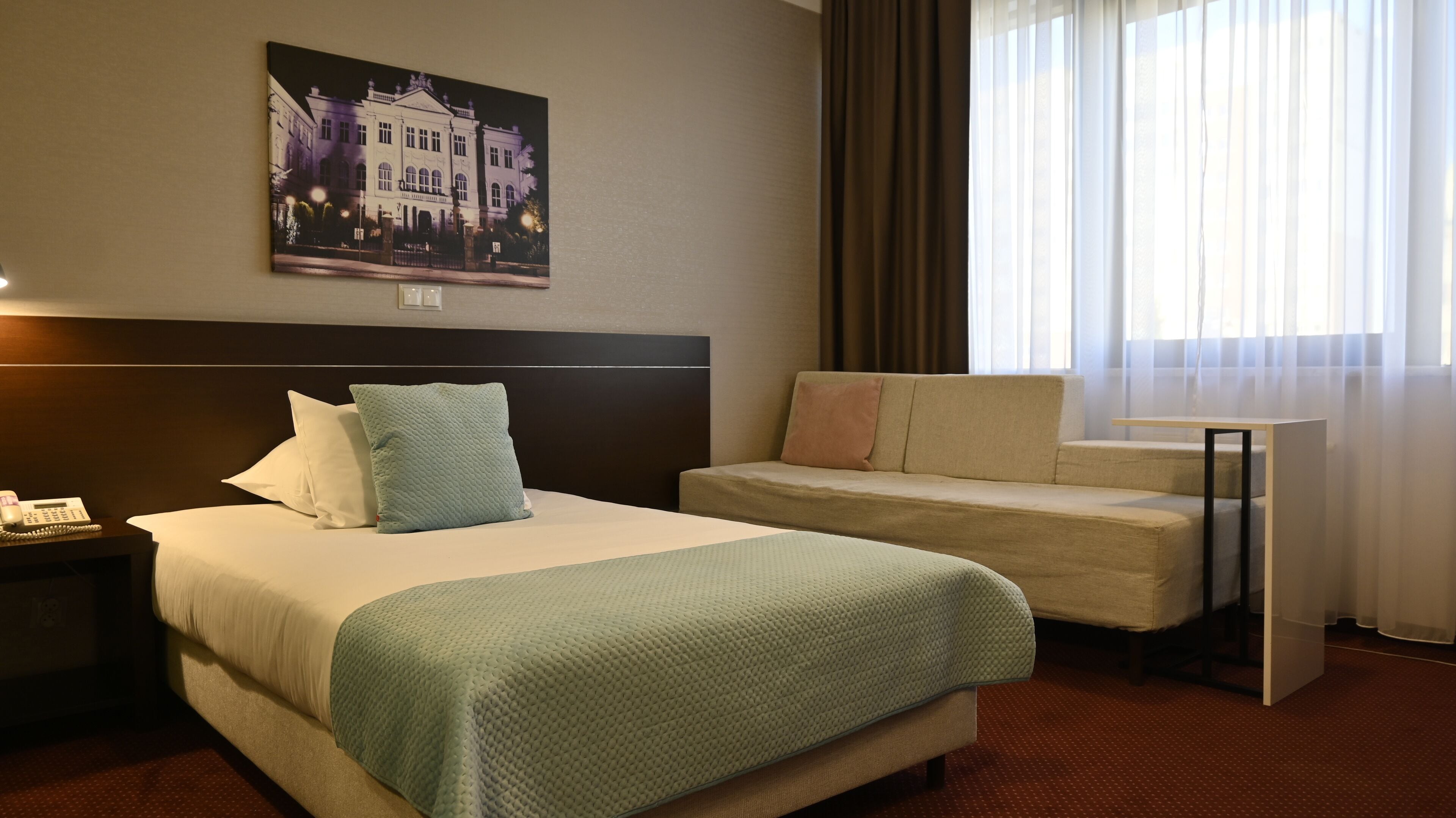 Une chambre d’hôtel avec un grand lit, un canapé, un bureau et un tableau représentant un bâtiment accroché au mur.