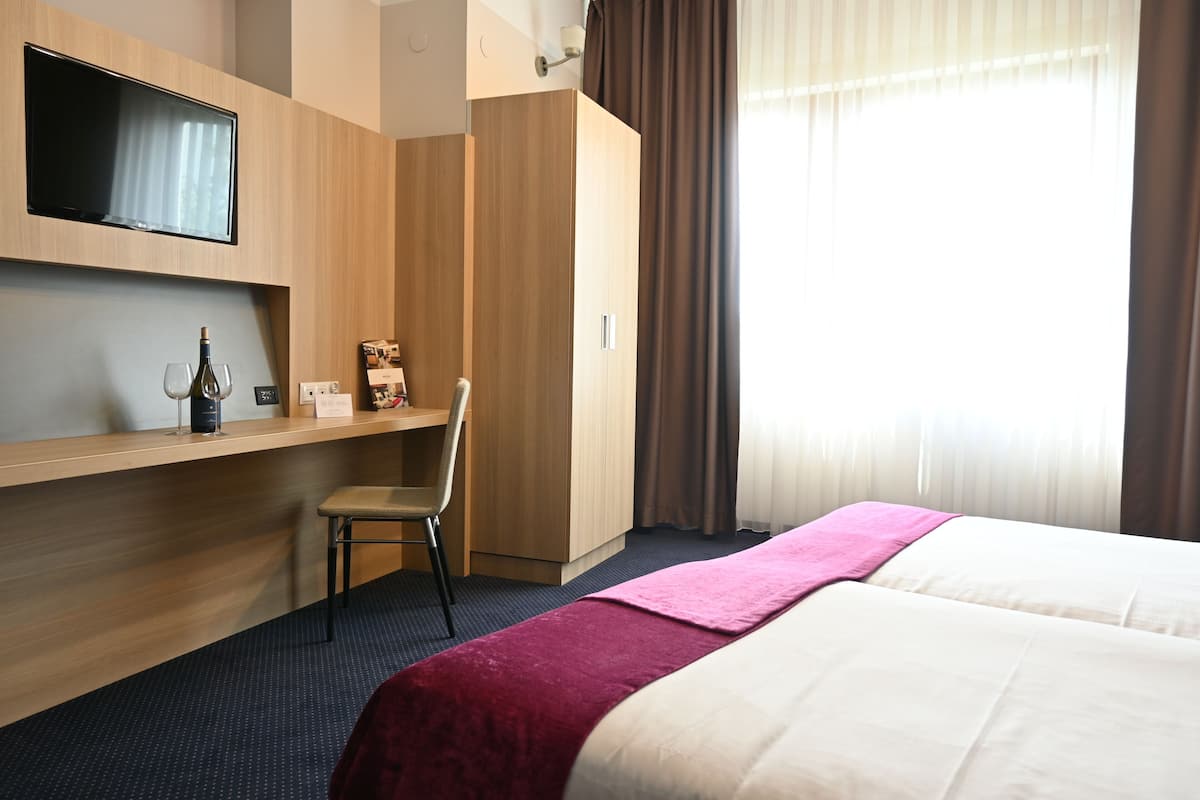 Une chambre d’hôtel comprenant un lit, un bureau avec une chaise, un téléviseur fixé au mur et une fenêtre avec des rideaux.