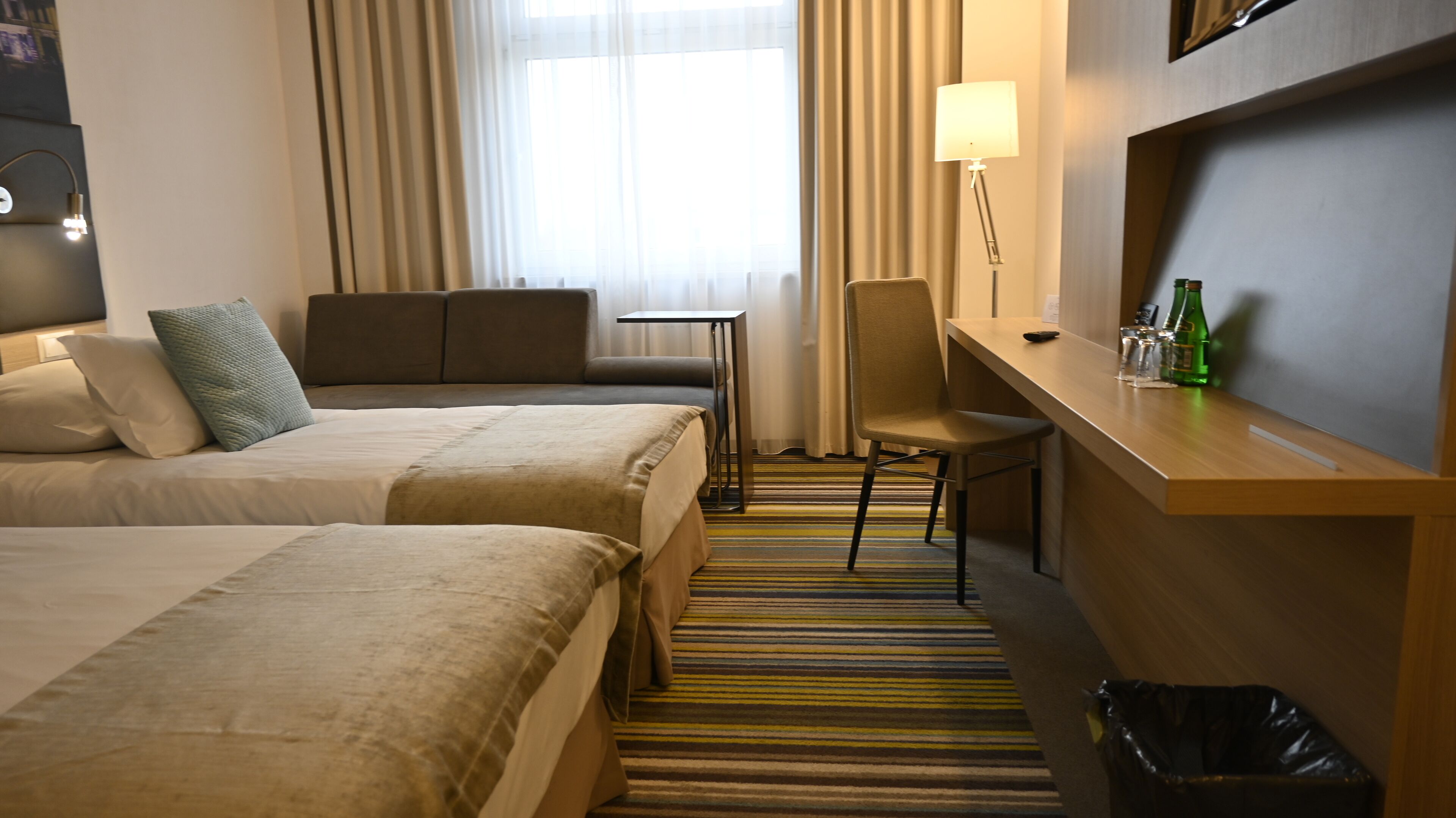 Une chambre d’hôtel avec deux lits, un bureau, une chaise, une poubelle et une lampe.