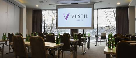 A conference room with a large screen displaying the Vestil Hotel logo, tables with chairs, and bottles of beer.