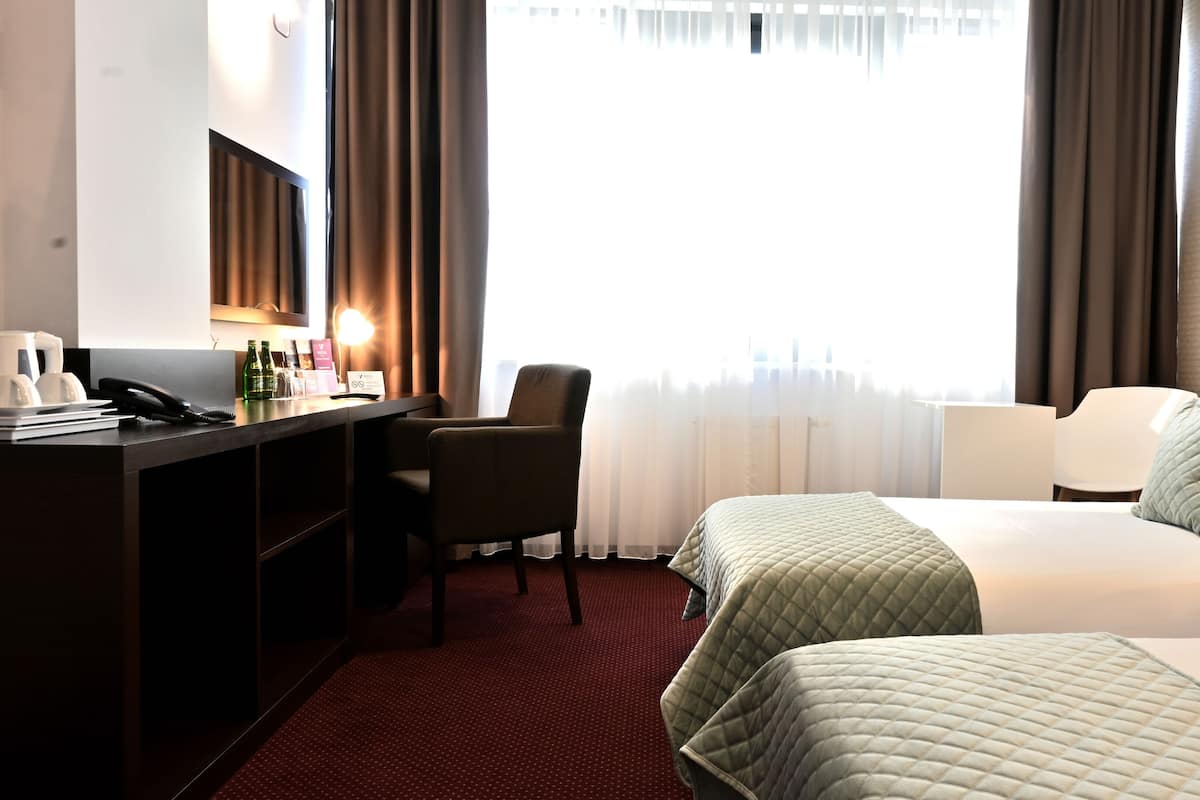 Une chambre d’hôtel équipée d’un bureau, de deux lits, d’une chaise et d’une fenêtre avec des rideaux.