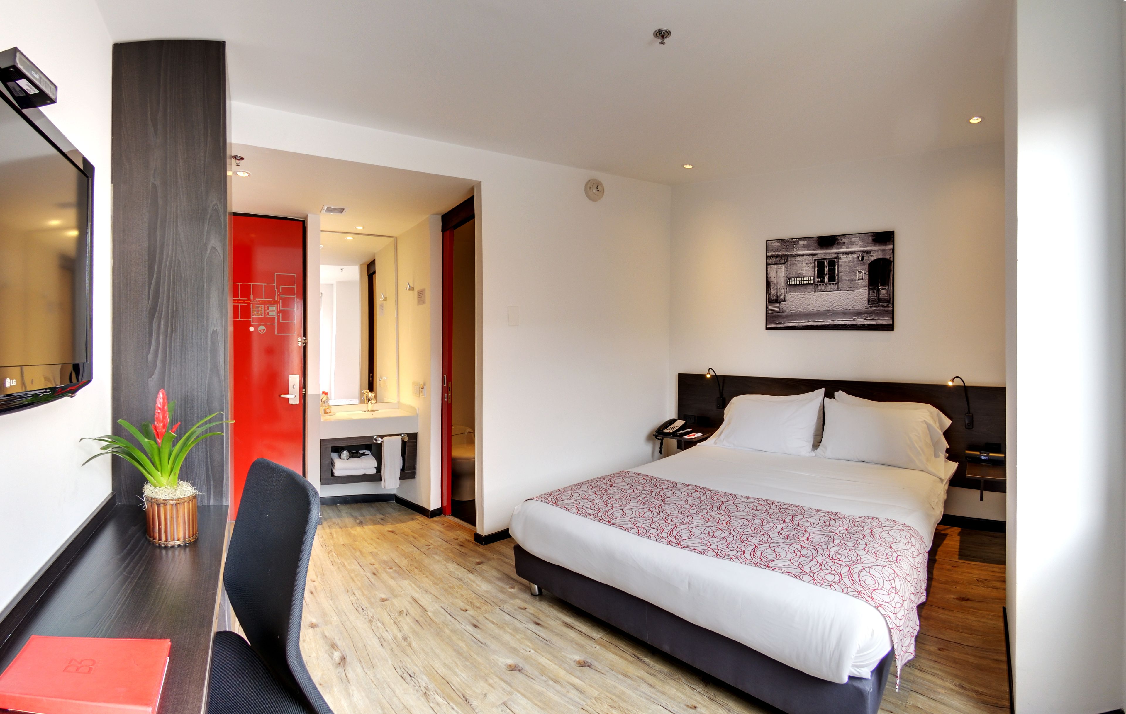 Habitación de hotel con cama, mesita de noche, silla y un pequeño escritorio con una planta.
