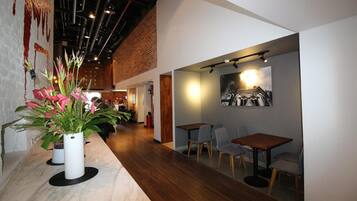 A modern interior with a long wooden counter, seating area with tables and chairs, and a brick wall.