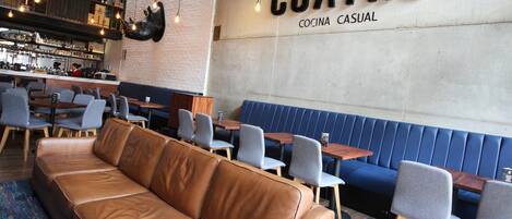 Un interno ristorante moderno con sedute in pelle, un'area bar e un muro con la scritta 'CUATRO COCINA CASUAL'.