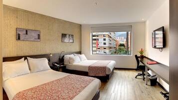 Habitación de hotel con dos camas, un escritorio, una silla, un televisor y una ventana con vistas a la ciudad.