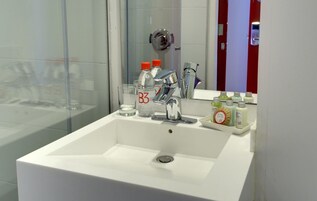 Un bagno moderno con un lavandino bianco, uno specchio e una cabina doccia in vetro.