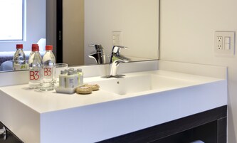 Un baño de hotel con un lavamanos blanco, un espejo y artículos de aseo, incluyendo botellas etiquetadas 'B3'.