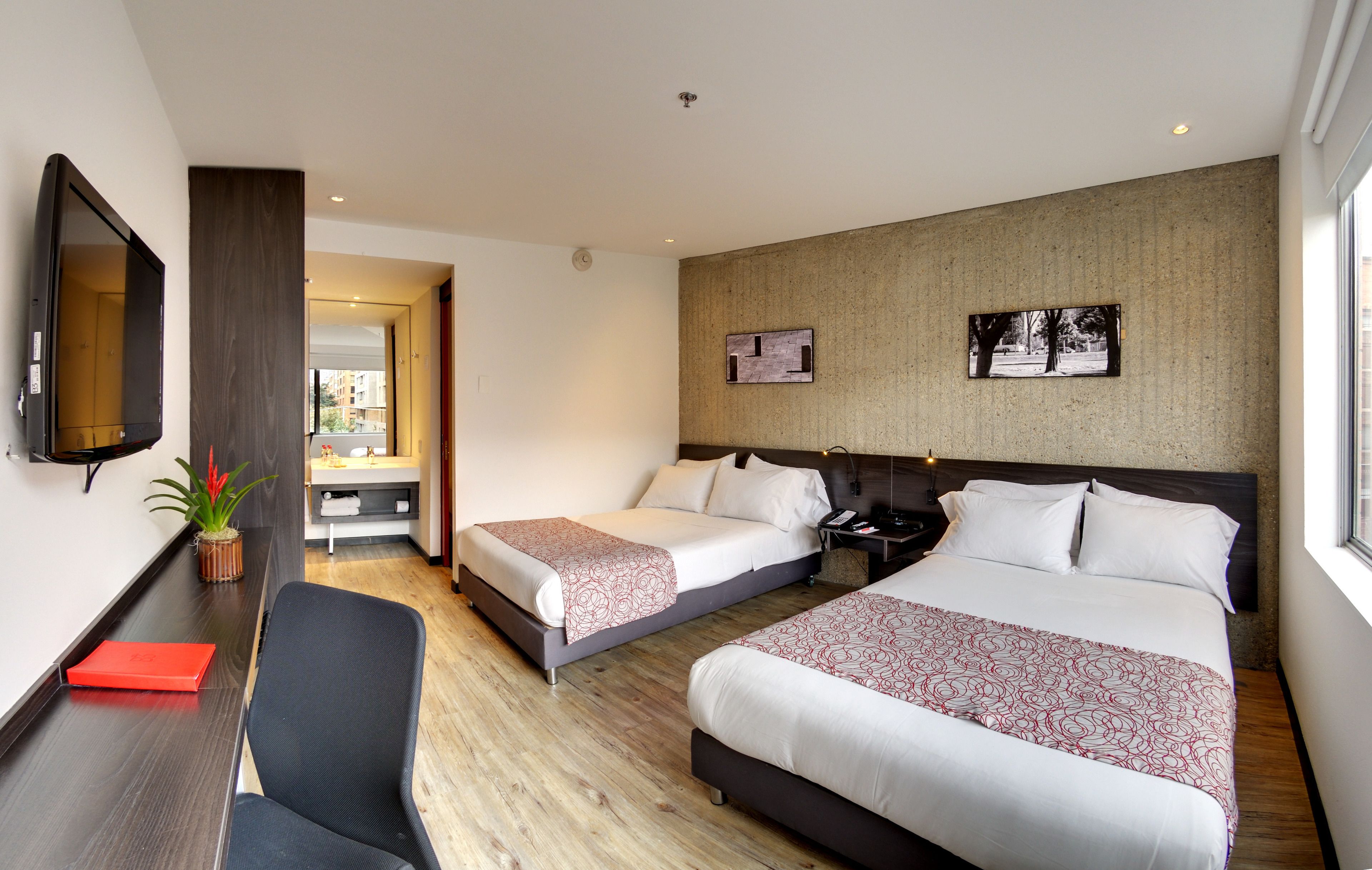 A hotel room with two beds, a desk with a chair, a TV, and a potted plant.