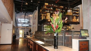 A modern bar area with a wooden counter, a vase with flowers, and a digital screen. - Hotel B3 Virrey (Bogotá)