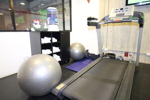 Un gimnasio con equipo de ejercicio, incluyendo una cinta de correr, pelotas de ejercicio y un dispensador de agua.