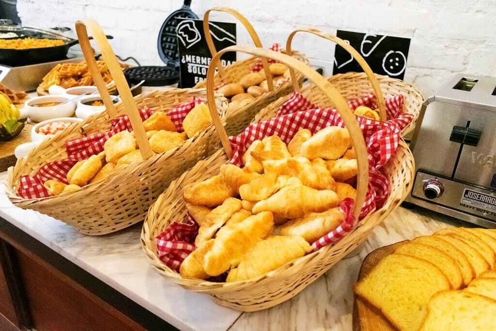 A buffet table with baskets of bread and pastries, a waffle maker, and a toaster.