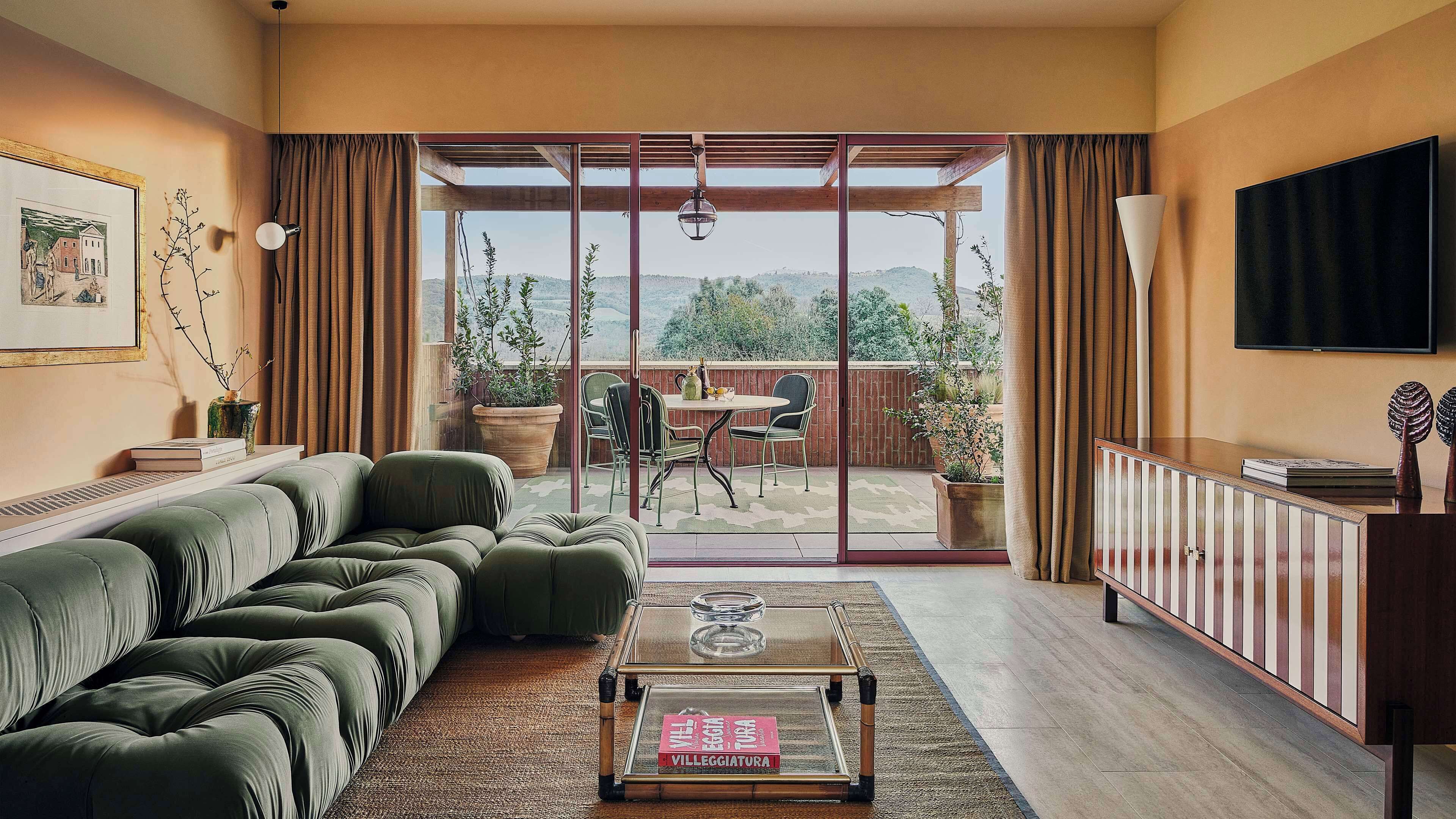 Ein Wohnzimmer mit einer Couch, einem Couchtisch mit einem Buch, einem Fernseher und Blick ins Freie.